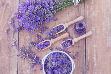 Top view of a bowl and wooden spoons with fresh lavender flowers, lavender essential oil and a bouquet of lavender on a brown wooden background.