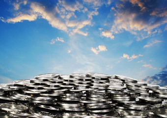 Mountain of coins against the sky with clouds. Symbol and metaphor of wealth, plenty, abundance, business. Photo collage