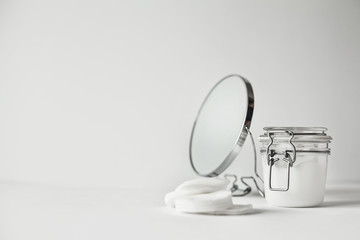 Beautiful minimalist conceptual all white composition - cotton pads, transparent jar and  round mirror, all white, with metallic details