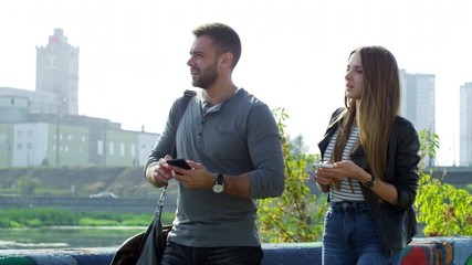 Medium shot of young Caucasian couple in casual clothes using smartphones when exploring city, man pointing at something in the distance - Powered by Adobe