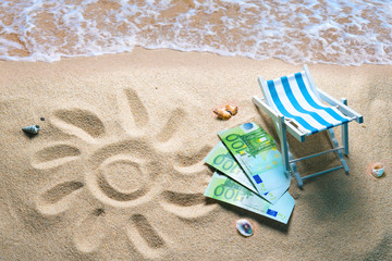 Deckchair with euro bills on a beach with a sun drawn on the sand