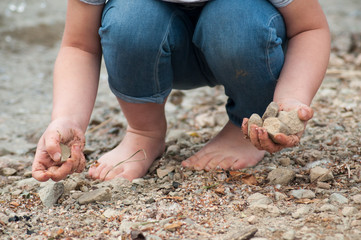 closeup of feet of child playing on the beach with stone