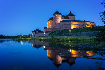 Fototapeta premium Beautiful view of lit 13th century Häme Castle and its reflections on lake Vanajavesi in Hämeenlinna, Finland, at night.