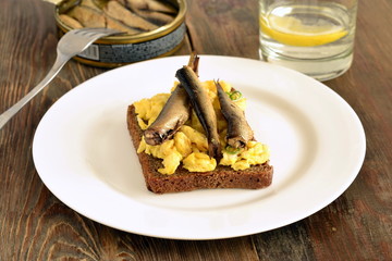 Sandwich with scrambled eggs and sprats on rye bread