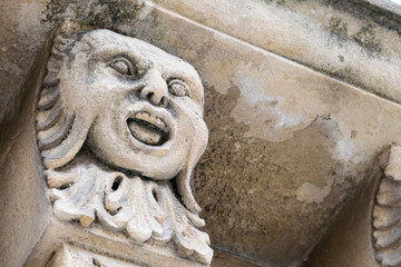 Closeup view of mascarons with funny faces under the balcony of a baroque palace in the province of Syracuse, Sicily