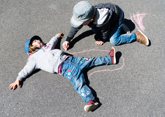 young blond boy drawing a chalk outline of a young girl on the street