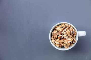 White cup full of walnuts on grey background. Above view