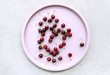 Cherries in pink round tray on concrete background.