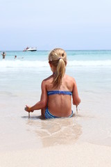 Fototapeta na wymiar Junges Mädchen sitzt am Strand und spielt mit nassem Sand und blickt ins Meer
