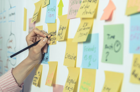 Business People Write Down An Important Note, Using On The Paper Stickers Post . The Hand Of A Woman Makes A Note Of The Idea, For Further Development.