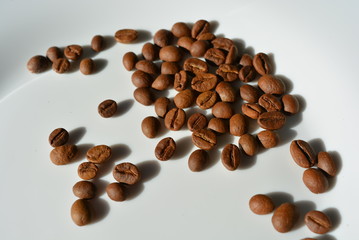 On a white glass plate laid and beautifully laid out a bunch of delicious and edible brown coffee beans