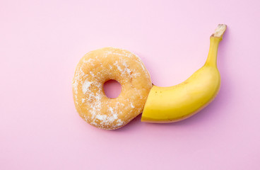 Fresh sweet donut and banana on pink background. Abive view