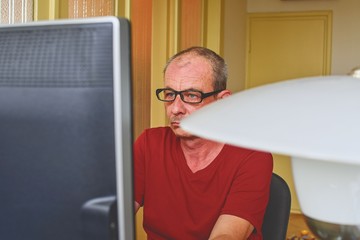 Fototapeta premium Middle aged man with glasses sitting at desk. Mature man using personal computer. Senior concept