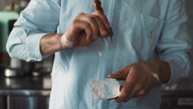 Bartender carves ice using ice pick