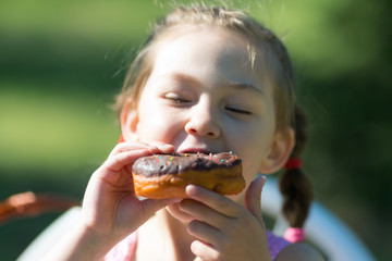 The child is eating a sweet donut. A beautiful girl bites a big sweet bun.