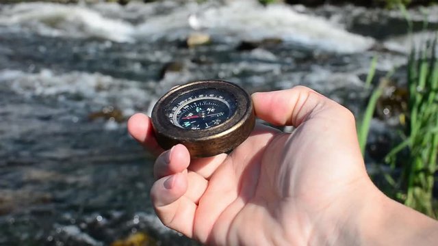 Man's hand holding a compass on the background of a stormy river.