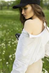 Beautiful girl photographer wearing a white shirt, beige trousers poses outdoors with a vintage camera against a background of meadow full of wild flowers