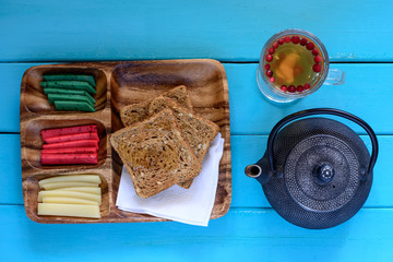 Toasts with three kinds of cheese on wooden plate, teapot and cup of tea.