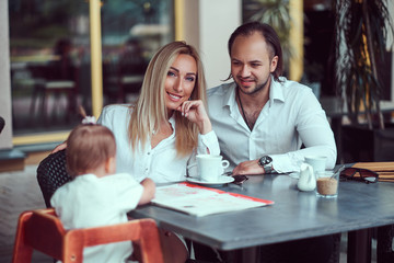 Family and people concept - happy mother, father and the little girl in outdoor cafe.