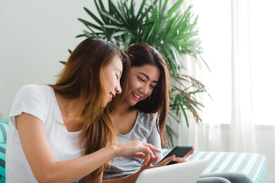 Beautiful young asian women LGBT lesbian happy couple sitting on sofa buying online using laptop a computer and phone in living room at home. LGBT lesbian couple together indoors concept.