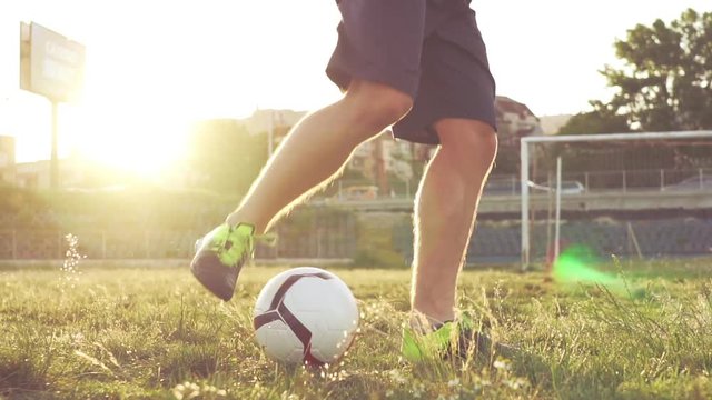 Slow motion football stunts. The football player throws the ball alternately with his feet. A teenager is playing on an abandoned football field at sunset on a sunny day in the summer. Football field