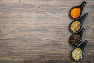 Obraz na płótnie Canvas different spices and herbs in spoons or bowls on a brown wooden background . Food and cuisine ingredients with copy space .Dried rosemary,black pepper,red paprika powder or Cayenne Pepper ,oregano