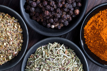 different spices and herbs in spoons or bowls on a brown wooden background . Food and cuisine ingredients  .Dried rosemary,black pepper,red paprika powder or Cayenne Pepper ,oregano close up