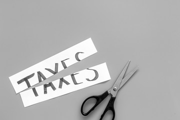 Cut taxes concept. Sciccors cut paper with word Taxes on grey background top view copy space