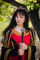 The Queen with a sword in her hands. Beautiful girl in the crown. Fantasy. Medieval black and red dress with gold embroidery.