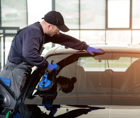 Automobile special workers replacing windscreen or windshield of a car in auto service station garage.