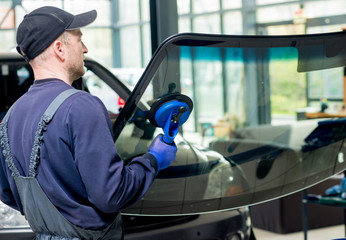 Automobile special workers replacing windscreen or windshield of a car in auto service station...