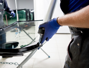 Automobile special workers replacing windscreen or windshield of a car in auto service station...