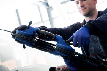 Automobile special workers replacing windscreen or windshield of a car in auto service station...