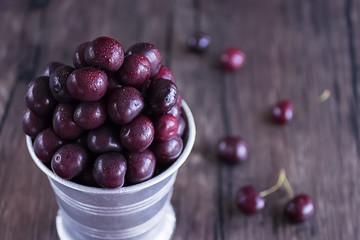 Ripe cherry in metal bucket on  dark wooden background.