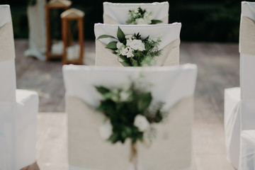 stylish chairs in white covers decorated with fresh flowers for wedding ceremony
