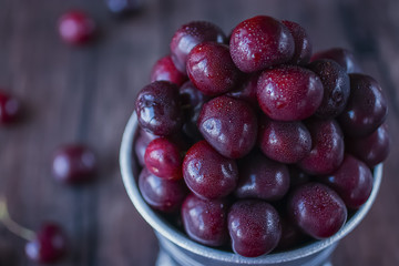 Ripe cherry in metal bucket on  dark wooden background.