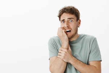 Studio shot of intense afraid handsome male feeling scared and shocked, biting fingernail and...