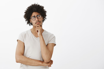 Portrait of handsome caucasian man with curly hair in glasses and t-shirt, frowning while looking...