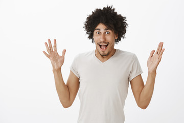 Studio shot of amazed and impressed excited male model with afro haircut and tanned skin, shaping object or shaking palms and smiling joyfully, sharing positive and great opinion over grey wall