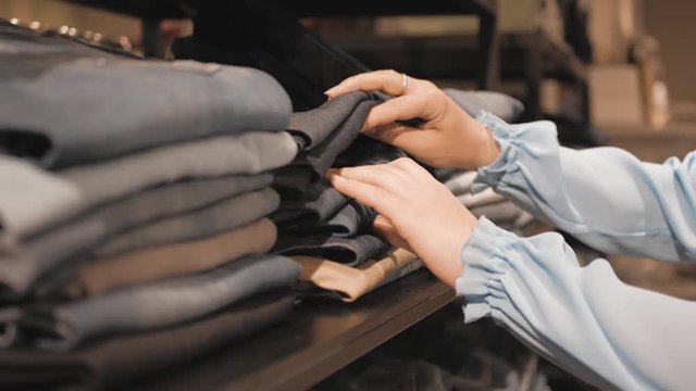 Woman choose new clothes in store , close-up of hands with denim or jeans on shop shelf