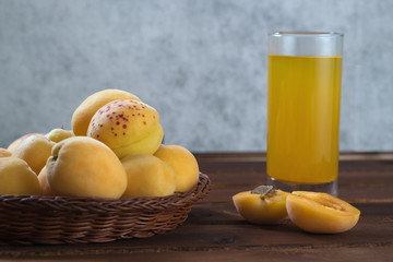 Juicy apricots in  wicker bowl lie on  dark wooden table and  glass of fresh apricot juice.