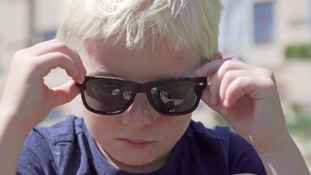 A sad boy with an abrasion on his face. The boy sits in glasses, removes sunglasses and he has a scar on his cheek