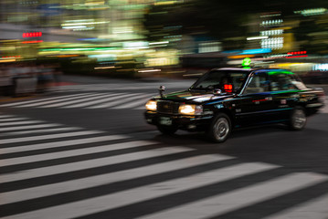 Fototapeta na wymiar Black taxi rushing in the streest of Tokyo at night with motion blur effect