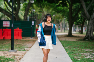 Portrait of a young and pretty Asian Chinese girl listening to music on her headphones as she goes strolling in the park.