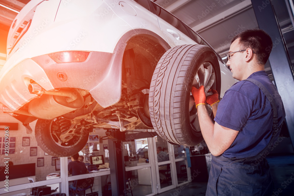 Wall mural Car mechanic inspecting wheel and suspension detail of lifted automobile at repair service station