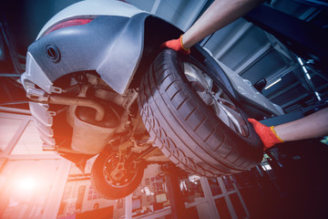 Car mechanic inspecting wheel and suspension detail of lifted automobile at repair service station