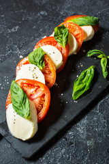 Caprese salad. Mozzarella cheese, tomatoes and basil herb leaves over stone table.