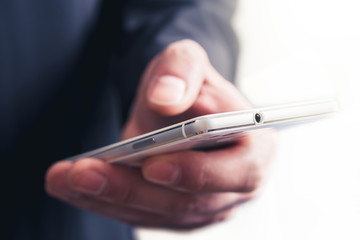 Close Up Of A Businessman Touching A Mobile Phone In Front Of A Bright Background