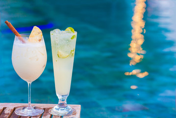 two perfect cocktails pina colada and mojito, pool background