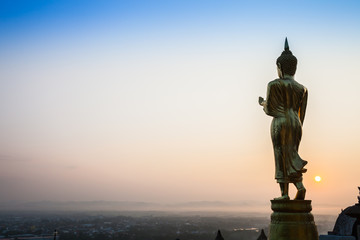Golden Buddha statue standing in front of colorful sky of sunset timing 